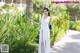 A woman in a white dress standing in front of a palm tree.