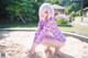 A woman in a purple and white plaid shirt crouching down in the sand.