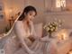 A woman in a wedding dress sitting on a bed with a bouquet of flowers.